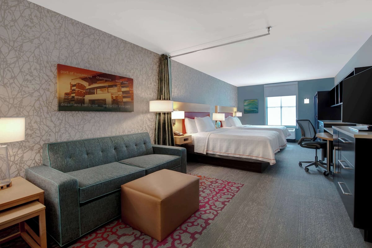 A hotel room with a sofa, a bed, a desk, and a television.