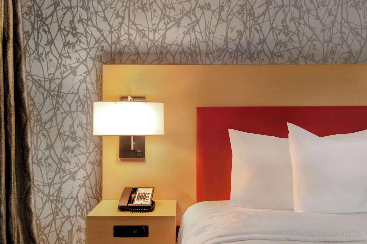 A hotel room with a bed, a bedside lamp, a telephone, and a nightstand.