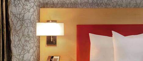 A hotel room with a bed, a bedside lamp, a telephone, and a nightstand.