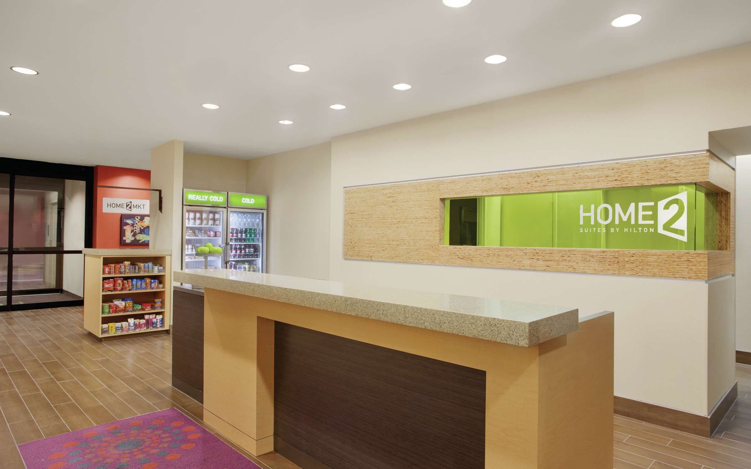 A hotel reception area with a counter, a refrigerator with beverages, and a shelf with snacks.