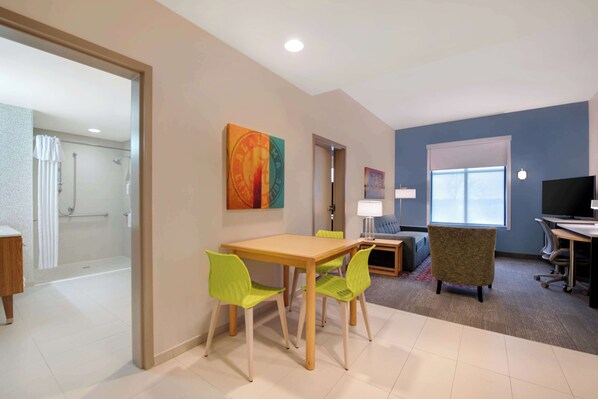Una habitación de hotel con baño, un área de comedor con mesa y sillas, un televisor y una ventana.