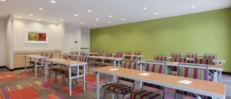 Une salle de conférence dotée de plusieurs tables et chaises, d’un mur d’accent vert et d’une fenêtre ornée d’un tableau.