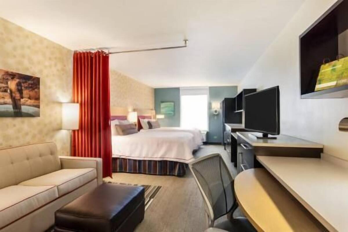 A hotel room with a bed, a desk, a TV, a sofa, and a window.
