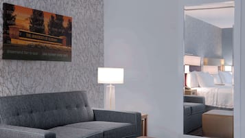 Quarto de hotel com um sofá cinzento, uma mesa de cabeceira com abajur e um espelho grande refletindo o quarto.