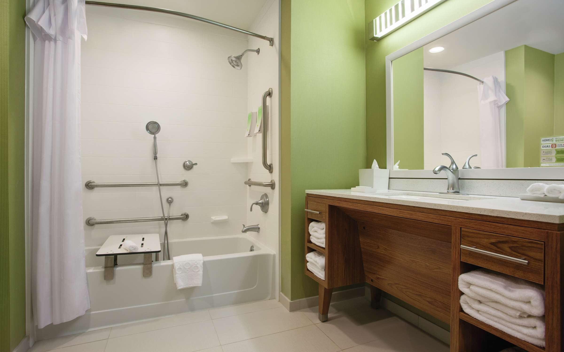A bathroom with a shower, grab bars, a bathtub, a vanity with a mirror, and a towel rack.