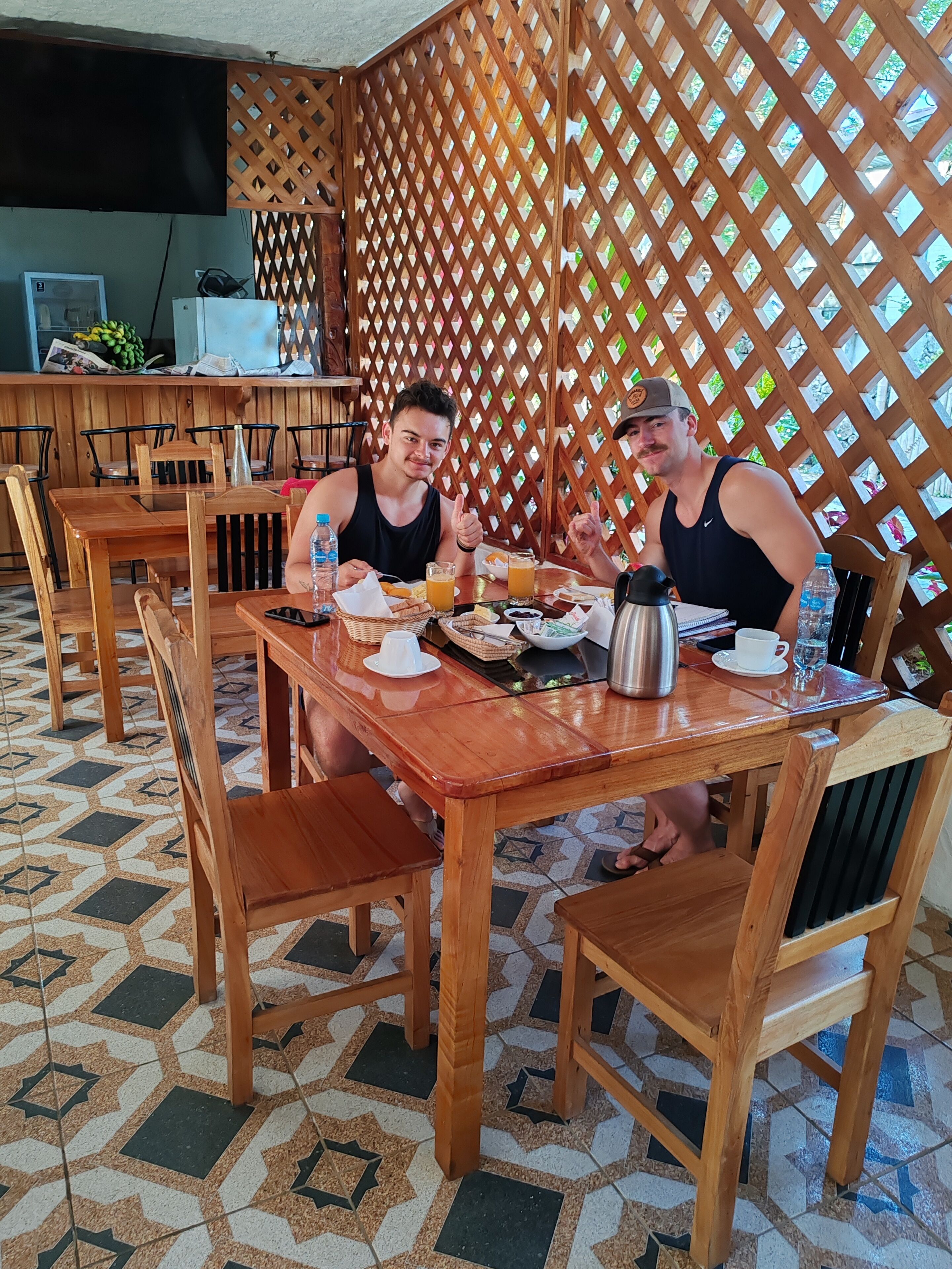Une table à manger en bois, des chaises, un sol carrelé et une cloison ajourée en arrière-plan.