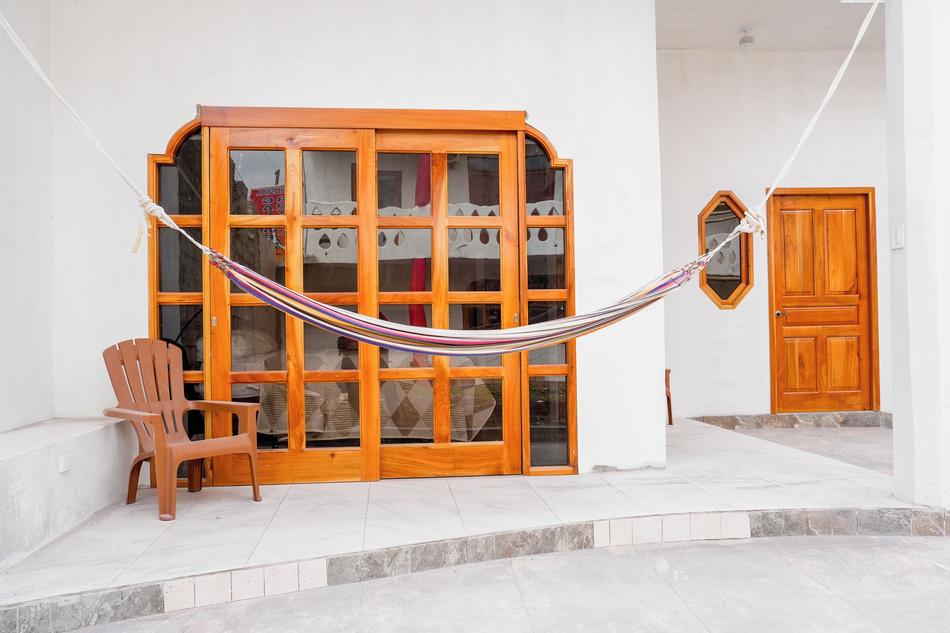 A hammock tied between two wooden doors, a wooden cabinet with glass doors, and a brown chair outside a building.