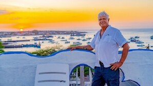 Un hombre está de pie en un balcón con vista a un puerto lleno de barcos al atardecer.