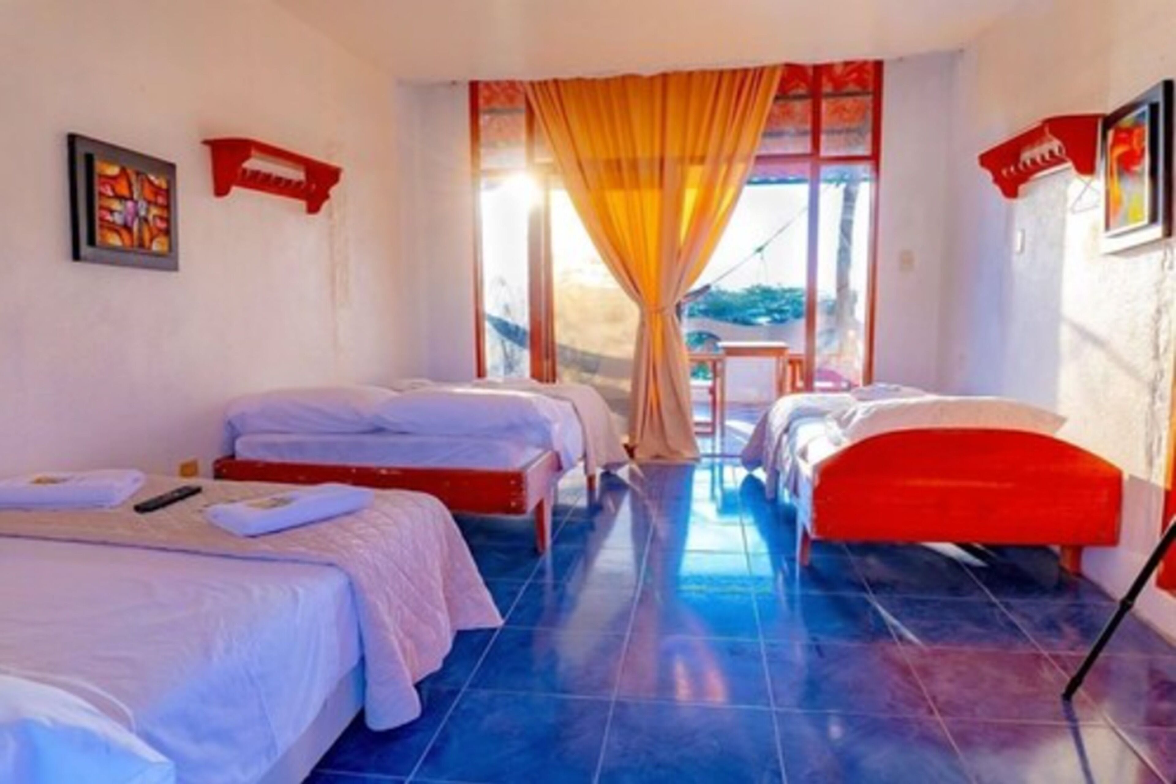 A room with two beds, a window with curtains, and a view of the outdoors.