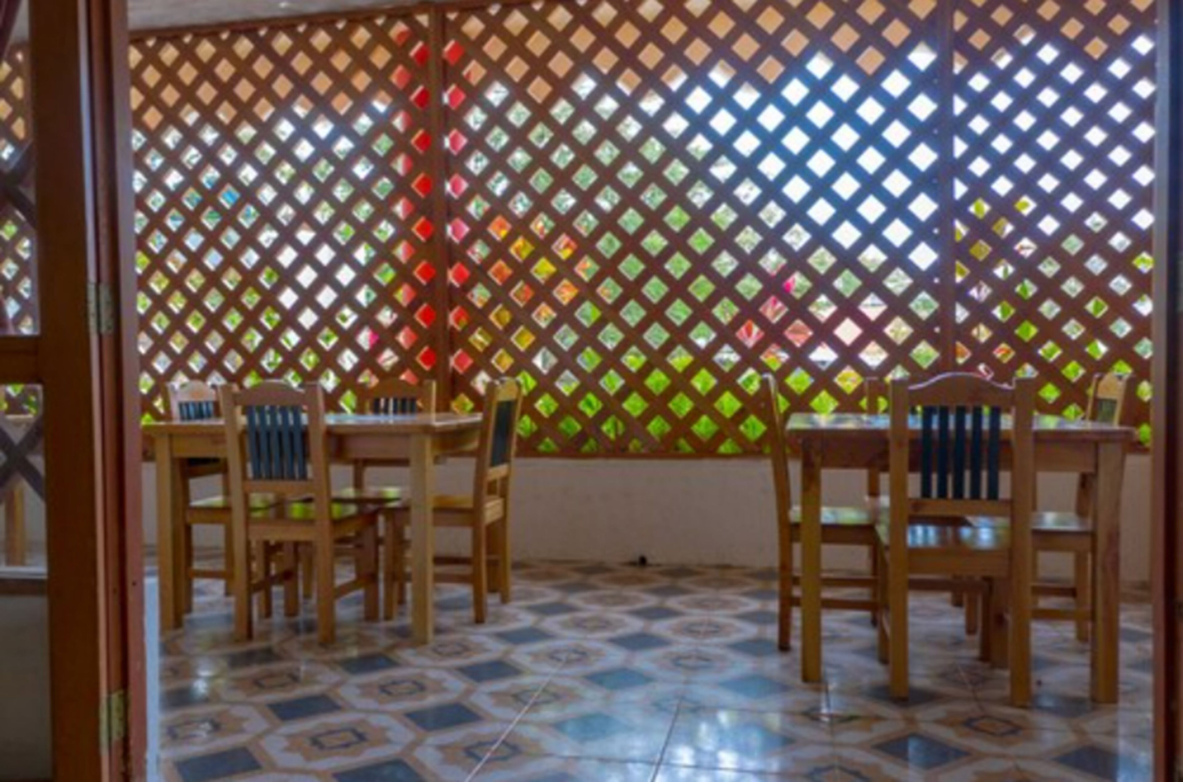 A room with a patterned floor, wooden chairs, and a lattice partition with colorful glass panels.