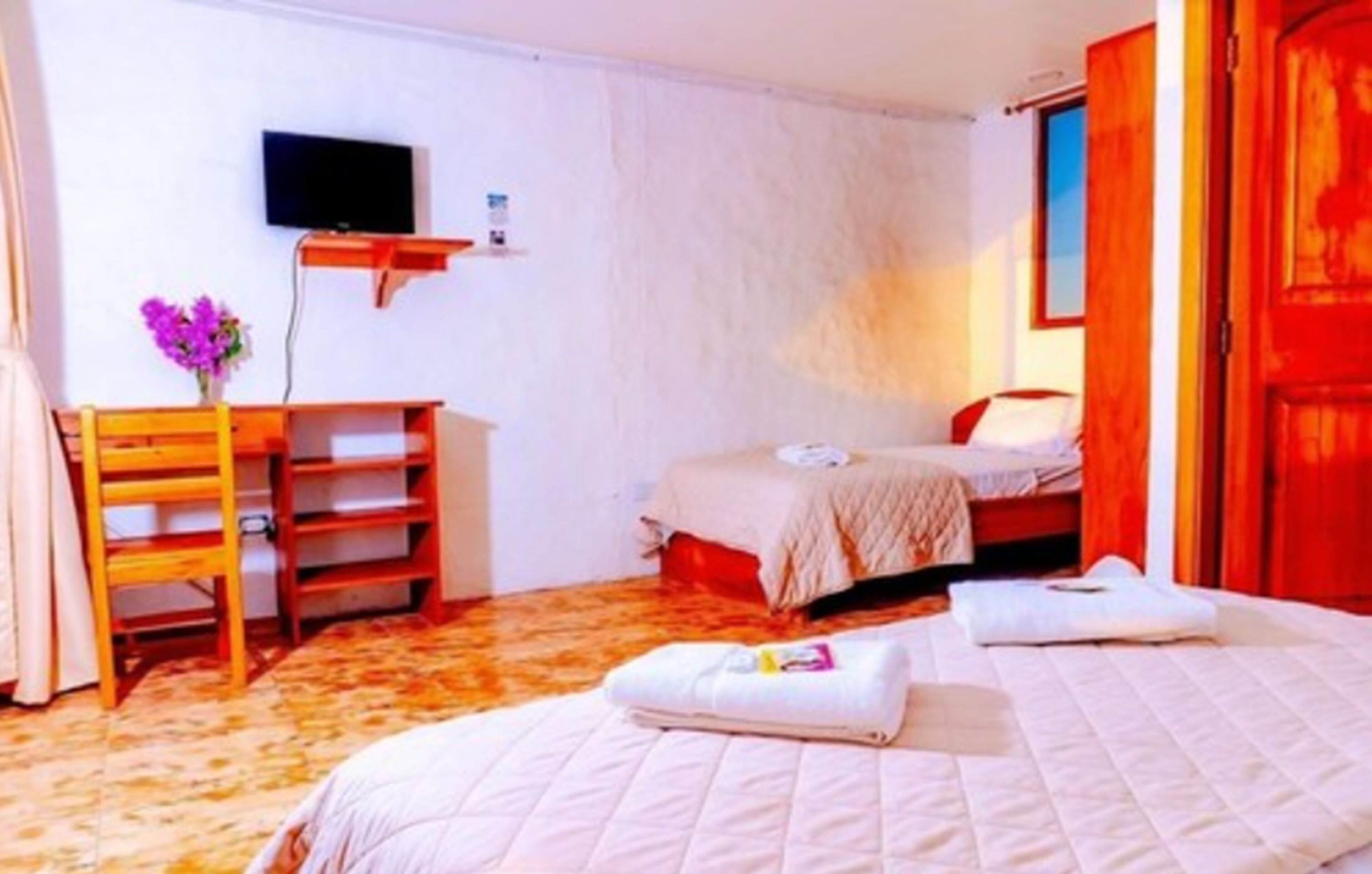 A bedroom with two beds, a TV mounted on the wall, and a wooden desk with a chair.