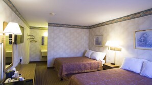 A hotel room with two beds, a bedside table with a lamp, a mirror, a painting on the wall, and a bathroom visible through an open door. - Value Inn Harrisburg - York (Etters)