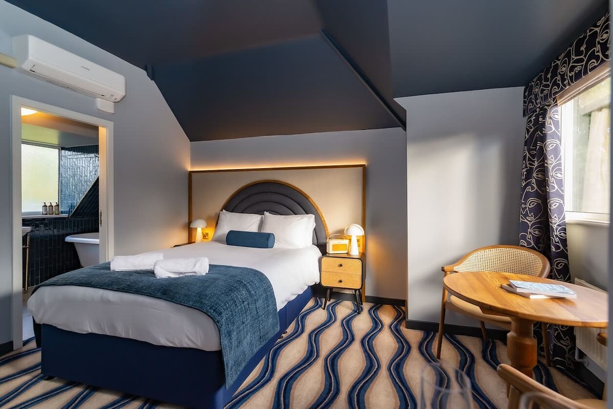 A hotel room with a bed, bedside table, lamp, chair, and a view of the outside.