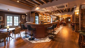 Zona de bar con mostrador de madera, taburetes y un refrigerador lleno de botellas.
