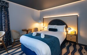 A hotel room with a large bed, two bedside tables, a chair, a lamp, and a patterned curtain. - The Anchorage (Poole)