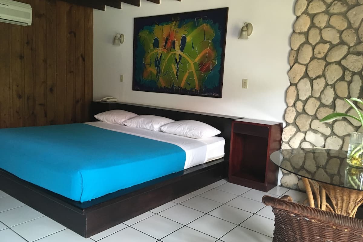 A room with a bed, a painting, a stone wall, and a wicker chair.