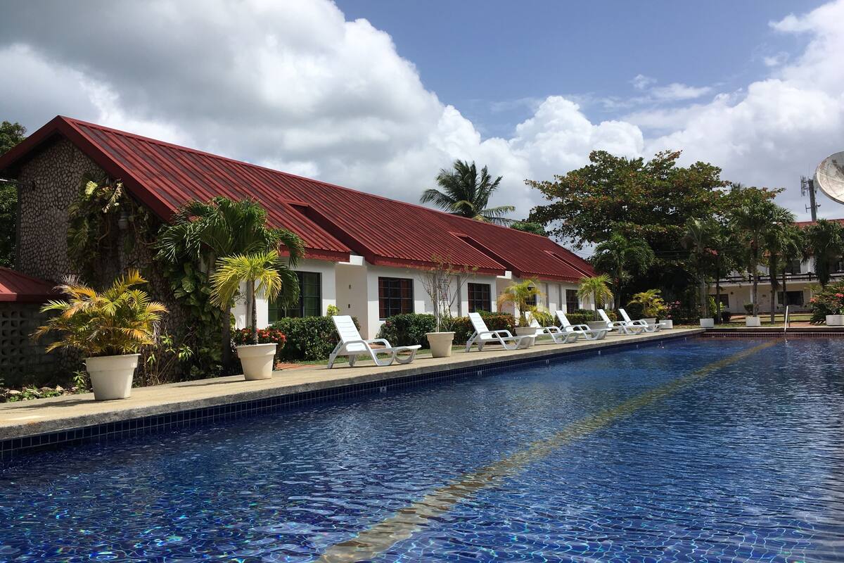 A poolside area with lounge chairs, a swimming pool, and a building with a red roof.