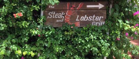 Un panneau en bois avec une flèche pointant vers la droite, indiquant la direction du restaurant « Steak and Lobster Grill ».