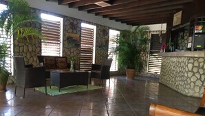 Un vaste espace intérieur doté d’un mur en pierre, d’un plafond en bois et d’un sol carrelé. On y trouve plusieurs plantes en pot, un canapé en osier et un banc en bois.