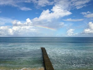 A pier extending into a calm sea with a rainbow in the distance.