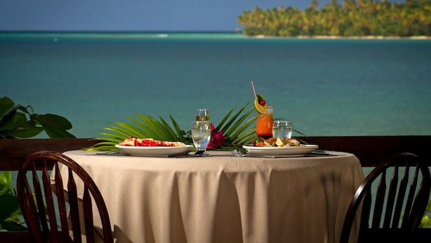 Une table dressée pour deux personnes, avec vue sur l’océan et une île lointaine.