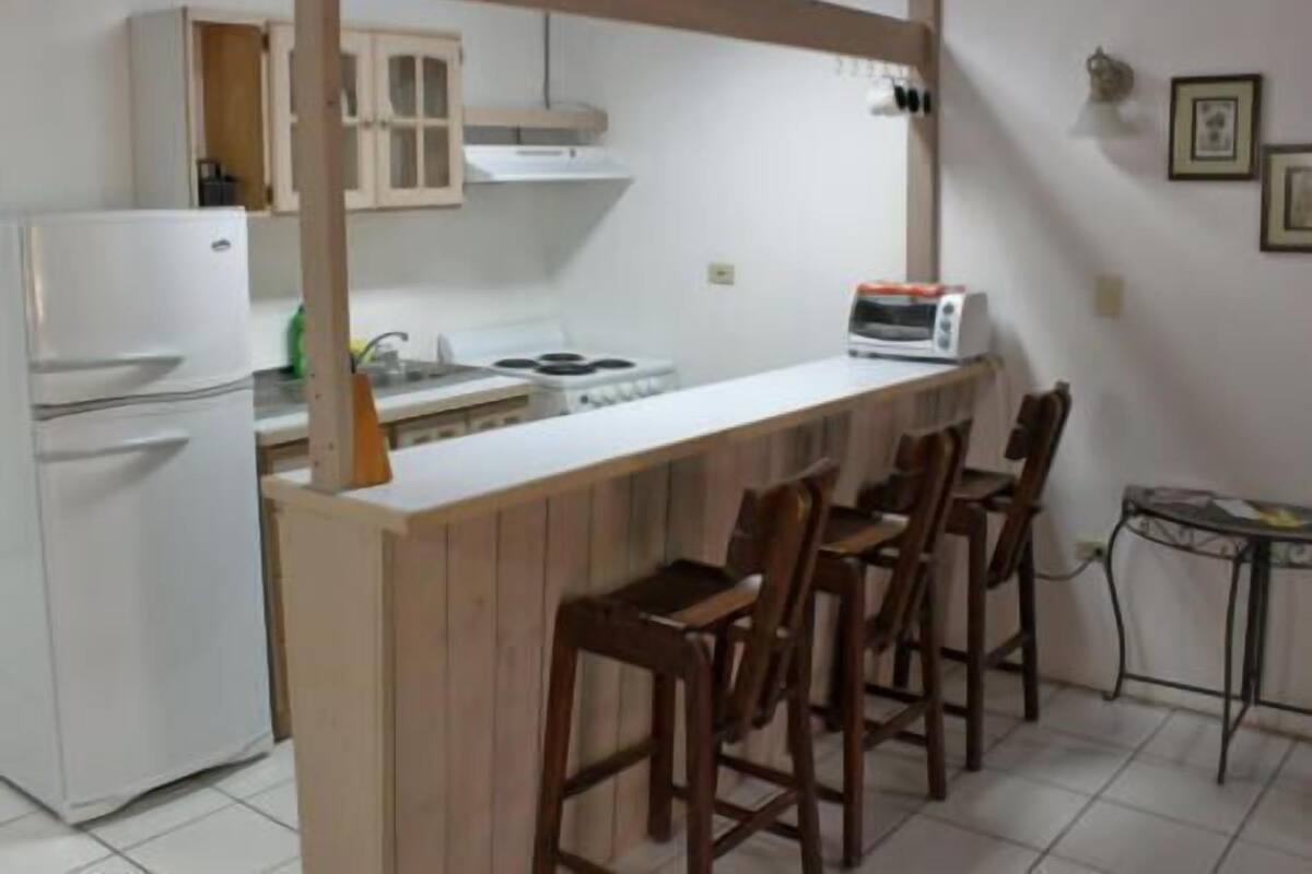 A kitchen with a white refrigerator, a stove, and a microwave. There are wooden chairs and a small table.