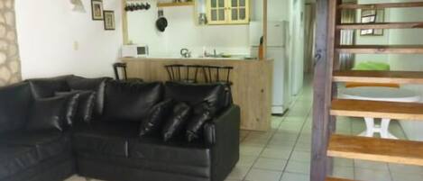 A living room with a black leather sofa, a wooden dining table, and a kitchen area with a wooden counter and cabinets.