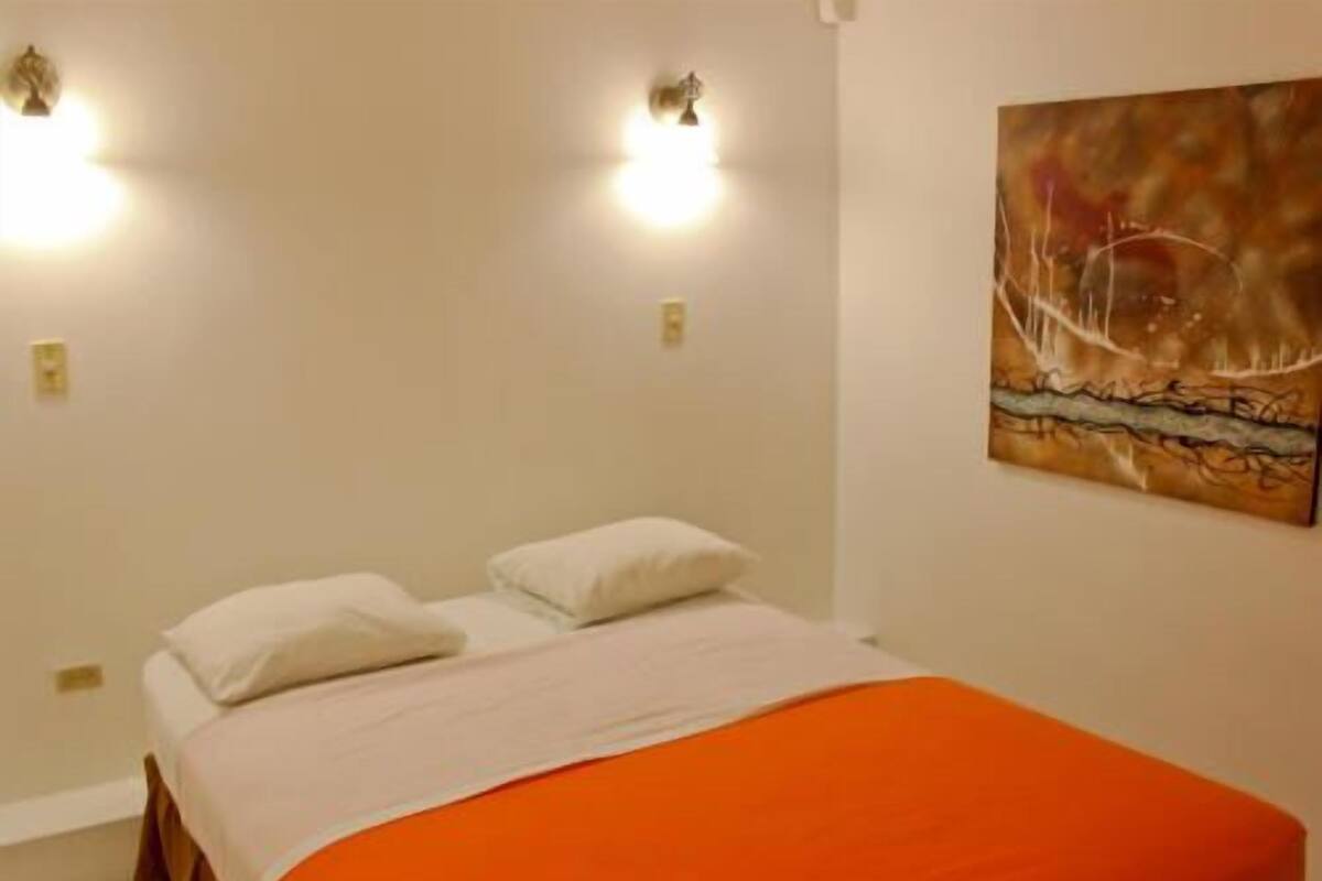 A bedroom with a bed, two wall-mounted lights, and a painting on the wall.