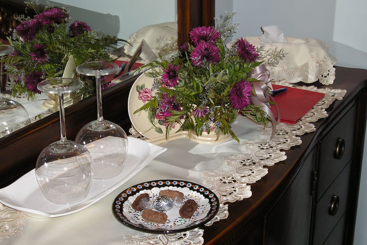 Une table recouverte d’une nappe en dentelle, un vase rempli de fleurs violettes, une assiette avec de la nourriture et un verre à vin.