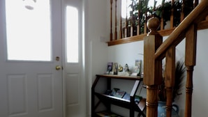 A staircase with wooden balusters, a white door with a brass doorknob, and a small shelf with books and decorative items. - Tucked Inn the Harbour Bed & Breakfast (Tay)