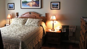 A bedroom with a bed, two bedside lamps, a nightstand, a dresser, and two framed pictures on the wall. - Tucked Inn the Harbour Bed & Breakfast (Tay)