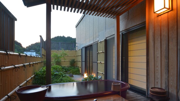 Een houten terras met een jacuzzi, een houten tafel en een klein krukje.