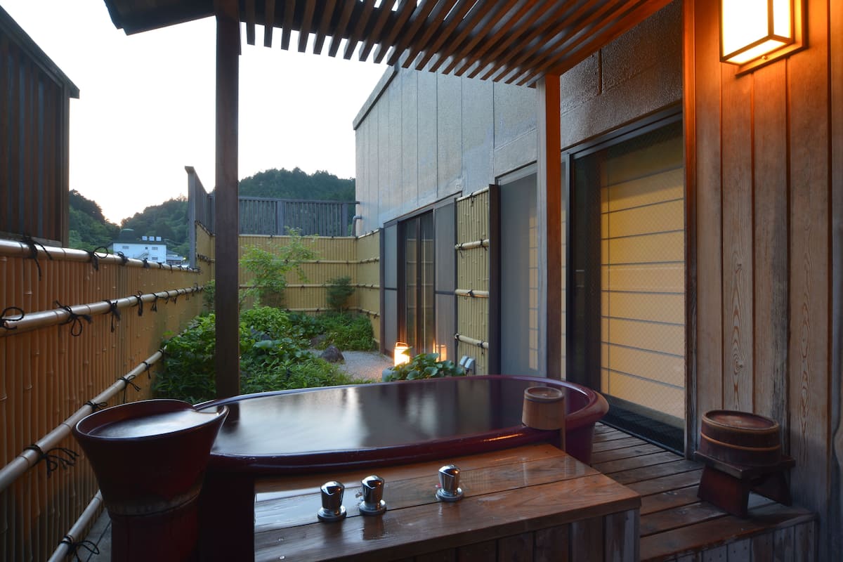 Une terrasse en bois avec un jacuzzi, une table en bois et un petit tabouret.