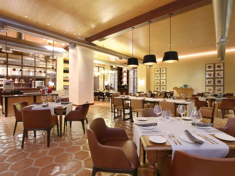 Un comedor amplio con varias mesas y sillas, una cocina al fondo e iluminación colgante.