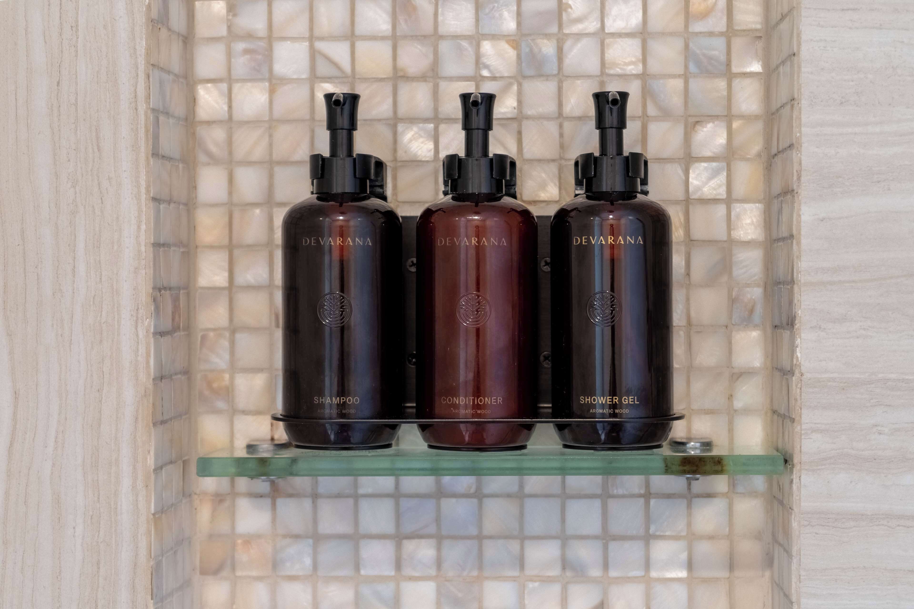 Three bottles of Devarana hair care products on a glass shelf against a tiled wall.