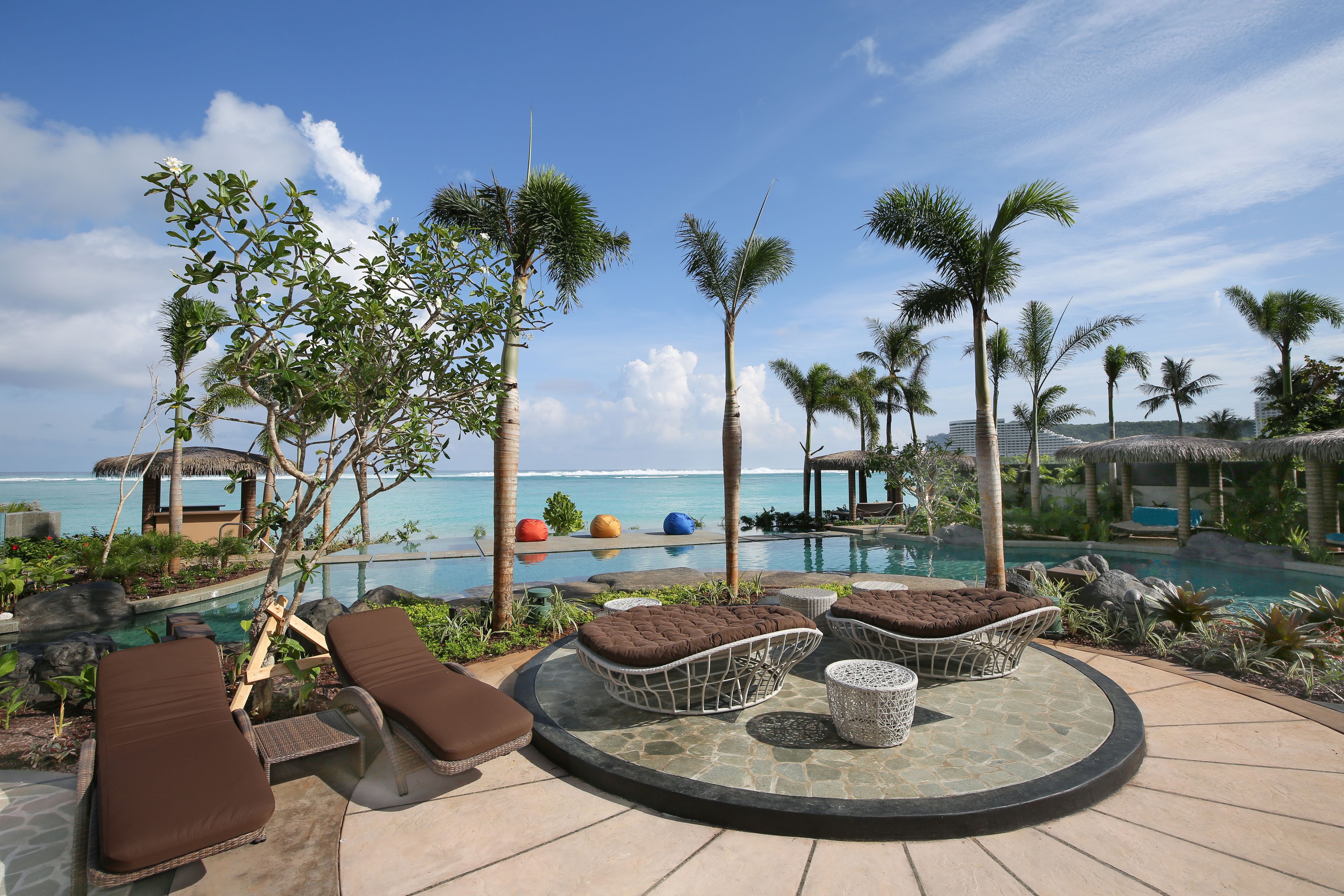Un espace aménagé au bord de la piscine, avec des chaises longues, une table ronde et une vue sur l’océan.