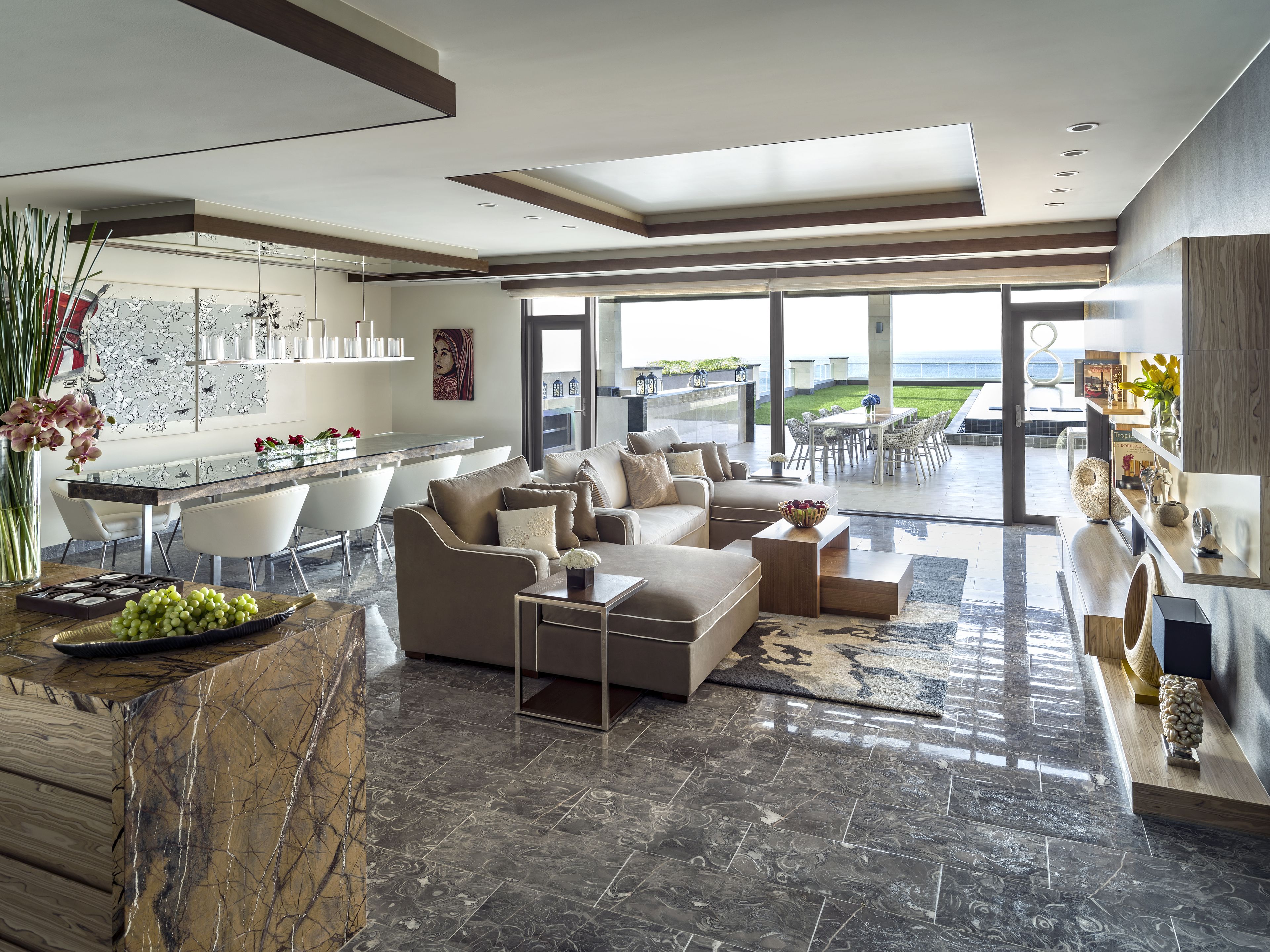 Amplia sala de estar con diseño moderno, que incluye un sofá grande, una mesa de comedor y una cocina con vistas al exterior.