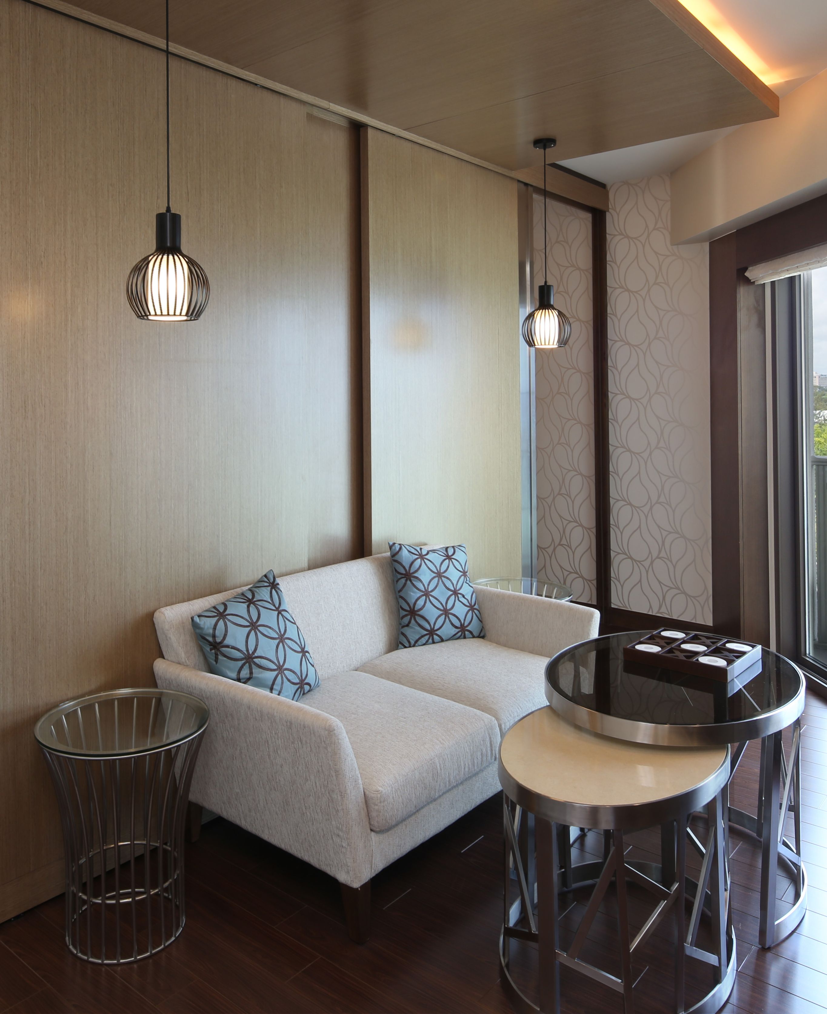 Una sala de estar moderna con sofá, cojines estampados, una mesa de centro de vidrio e iluminación colgante.