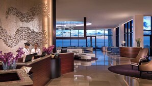 A modern hotel lobby with a reception desk, seating area, and large windows offering a view of the ocean.