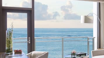A room with a view of the ocean, a dining table with a vase of flowers, and a round table with a glass top.