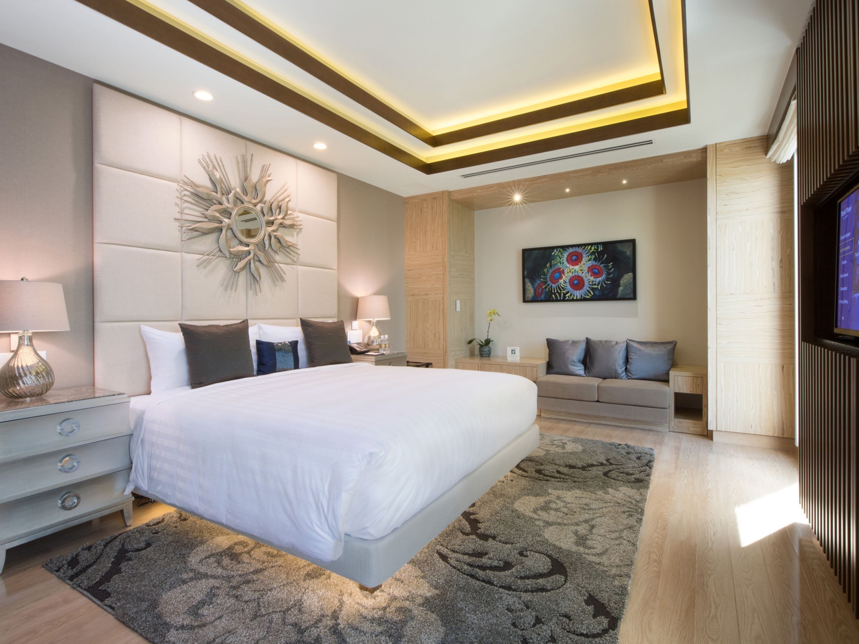 A modern bedroom with a large bed, a nightstand, a sofa, and a TV.