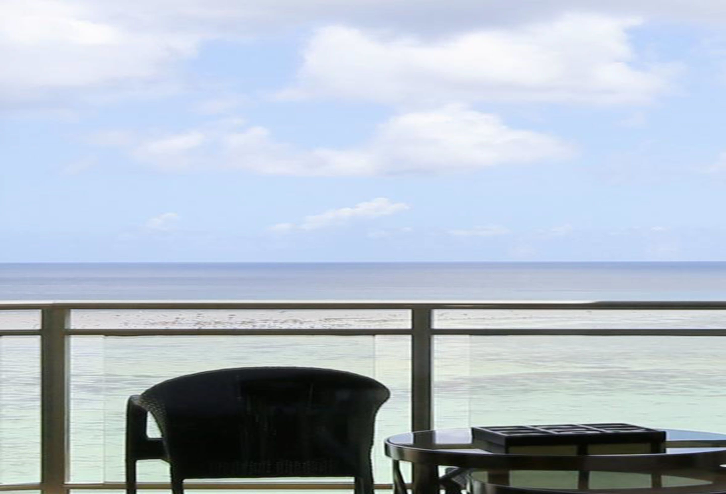 Un balcon avec vue sur l’océan, une chaise et une petite table.