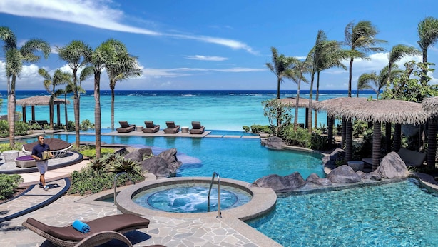 A resort pool area with lounge chairs, a hot tub, and a view of the ocean.