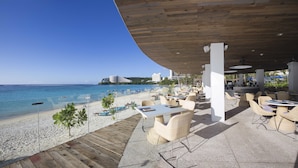 An outdoor seating area with tables and chairs overlooking a beach and ocean.