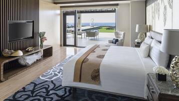Una habitación de hotel moderna con una cama grande, televisión, balcón con vista al mar y zona de comedor.