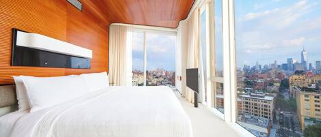 A modern hotel room with a large bed, a TV, and a city view.
