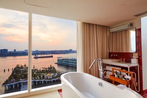 A modern bathroom with a large bathtub, a vanity with a mirror, and a view of a river with boats and a bridge.