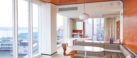 A modern hotel room with a large window, a seating area, and a kitchenette.