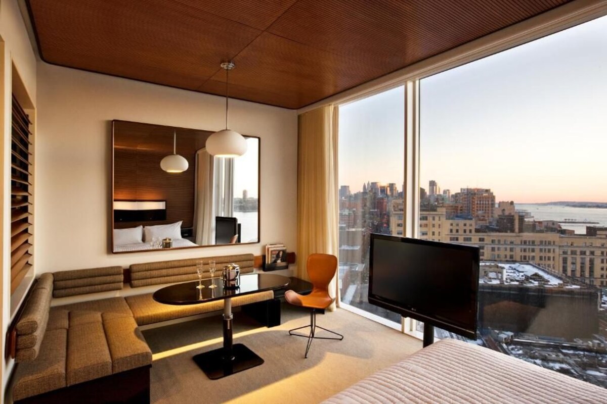 Een moderne hotelkamer met een groot raam, een bank, een televisie en uitzicht op de stad.