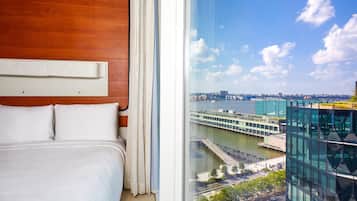 Ein Hotelzimmer mit einem großen Bett, einem Holzkopfteil und Blick auf eine Stadtlandschaft durch ein großes Fenster.